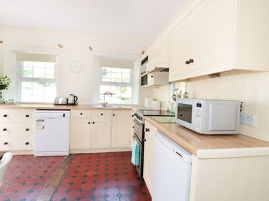 A kitchen with white cabinets two windows a microwave a stove a toaster and kettles at School House in Builth Wells