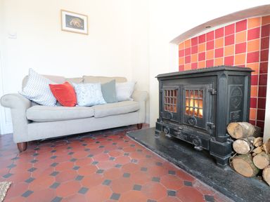 A sitting area with a beige sofa with cushions and a black wood-burning stove with logs beside it at School House in Builth Wells