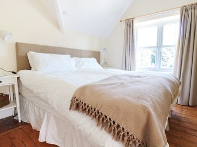 A bedroom with a bed covered with white bedding and a beige throw near a window with curtains at School House in Builth Wells