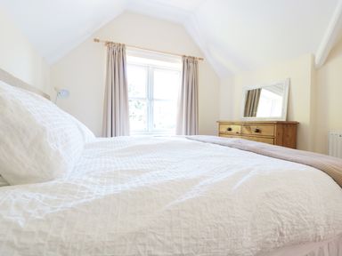 A bedroom with a bed covered in white bedding a window with curtains and a wooden dresser with a mirror at School House in Builth Wells