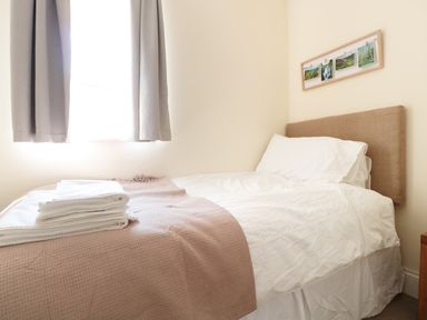 A bedroom with a single bed white bedding towels on bed a window with curtains and framed pictures on wall at School House in Builth Wells