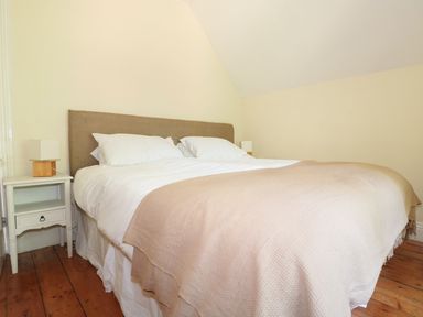 A bedroom with a bed with beige headboard white bedding and beige blanket with white bedside tables and lamps at School House in Builth Wells