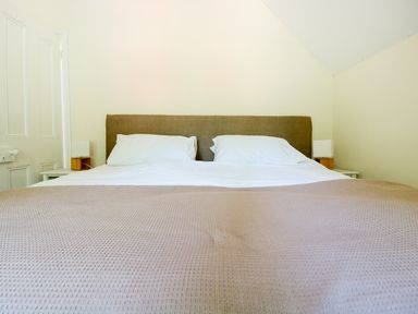 A bed with white pillows and sheets and a beige blanket in a bedroom at School House in Builth Wells