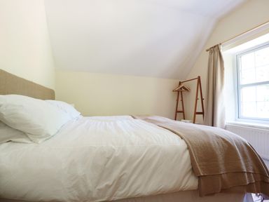 A bedroom with a bed with white sheets and a brown blanket next to a window with beige curtains at School House in Builth Wells
