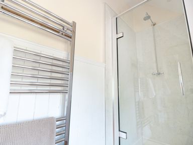 A bathroom with a glass shower enclosure and a chrome towel radiator with towels at School House in Builth Wells