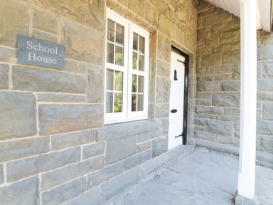 Stone exterior wall with a white window and a white door beside a sign reading School House at School House in Builth Wells