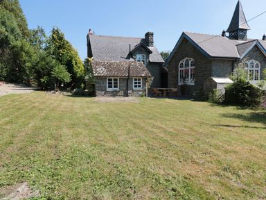 A green lawn in front of stone buildings with pitched roofs and windows at School House in Builth Wells