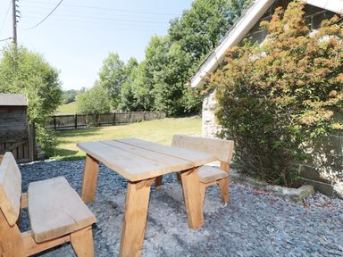 An outdoor area with a wooden table and benches next to a stone wall with a climbing plant at School House in Builth Wells