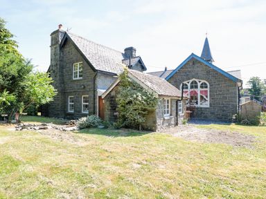 A stone house with multiple sections surrounded by grass and trees at School House in Builth Wells