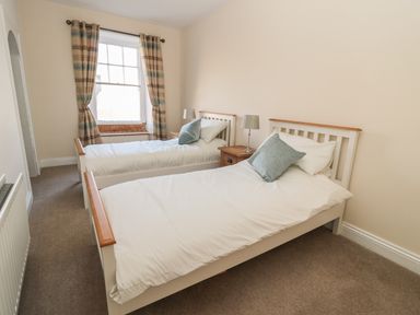 A bedroom with two single beds a window with curtains and bedside tables with lamps at Hare & Hounds House in Allendale