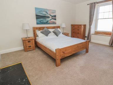 A bedroom with a wooden double bed two bedside tables with lamps a wooden chest of drawers a window with curtains and a mountain landscape picture above the bed at Hare & Hounds House in Allendale