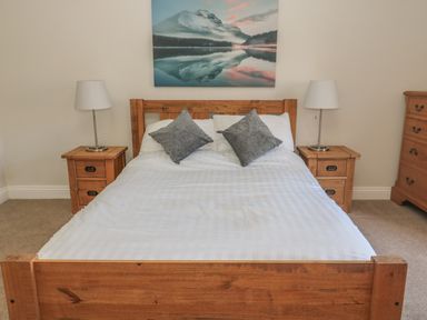 A bedroom with a wooden bed with white bedding two gray pillows two wooden nightstands each with a lamp and a dresser on the right wall with a landscape painting above the bed at Hare & Hounds House in Allendale
