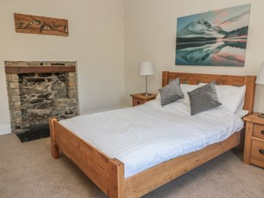 A bedroom with a wooden bed frame white bedding gray pillows two wooden bedside tables with lamps and a stone fireplace at Hare & Hounds House in Allendale