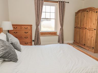 A bedroom with a wooden bed a wooden wardrobe a wooden chest of drawers and a window with curtains at Hare & Hounds House in Allendale