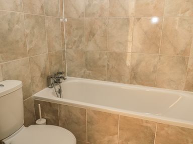 A bathroom with a bathtub and a toilet with beige tiled walls at Hare  Hounds House in Allendale