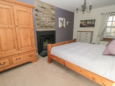 A bedroom with a wooden bed a wooden wardrobe a white chest of drawers and a stone fireplace at Hare & Hounds House Allendale