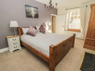 A bedroom with a wooden bed with white bedding and purple pillows two bedside tables with lamps and a window with cream curtains at Hare & Hounds House in Allendale