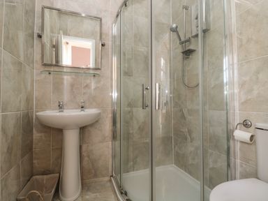 A bathroom with a pedestal sink mirror glass shower enclosure and toilet with tiled walls at Hare & Hounds House in Allendale