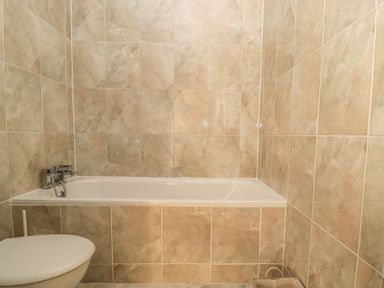 A bathroom with a bathtub, toilet, and beige wall tiles at Hare & Hounds House in Allendale