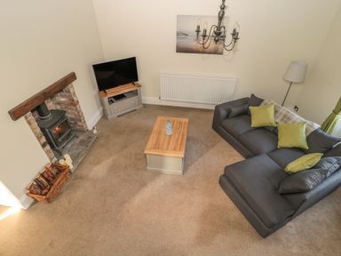 A living room with a gray sofa and green cushions a coffee table a TV on a stand a fireplace and a floor lamp at Hare & Hounds House in Allendale