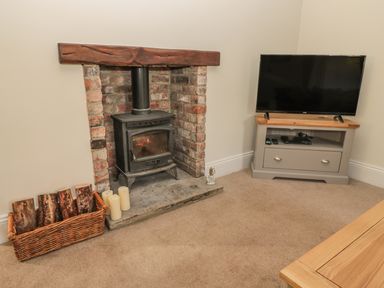 A room with a wood burning stove and a television on a stand at Hare & Hounds House in Allendale