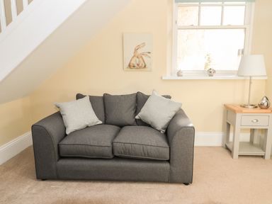 A sitting area with a gray sofa cushion pillows side table lamp window and rabbit painting at Hare & Hounds House in Allendale