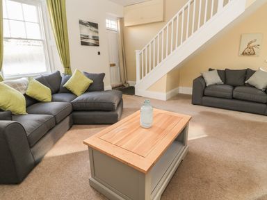 A living room with two grey sofas with cushions a wooden coffee table and a staircase at Hare amp Hounds House in Allendale
