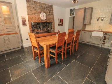 A kitchen with wooden dining table and chairs stone fireplace and grey cabinets at Hare & Hounds House in Allendale