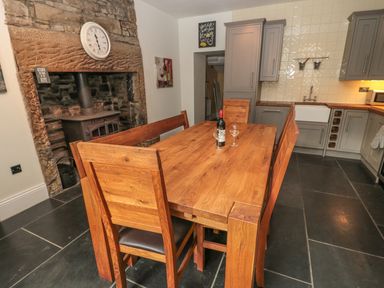 A kitchen with wooden dining table and chairs and a stone fireplace at Hare & Hounds House in Allendale