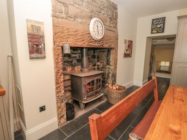 A kitchen area with a wood-burning stove in a stone fireplace and a wooden bench at Hare & Hounds House in Allendale