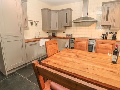 A kitchen with wooden dining table and chairs grey cabinets and tiled walls at Hare & Hounds House in Allendale