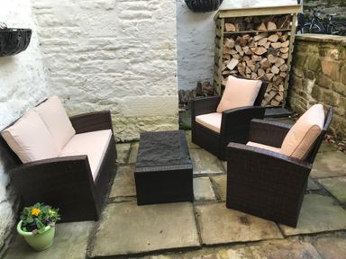 An outdoor patio with two armchairs a loveseat and a small table on stone pavement next to a stack of firewood and a potted plant at Hare & Hounds House in Allendale