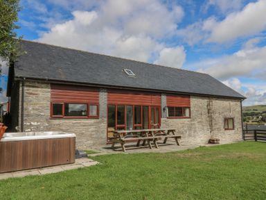 An outdoor patio area with a hot tub and seating at Glanyrafon St Harmon