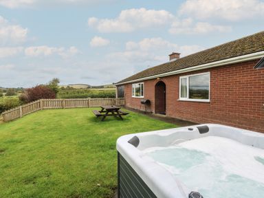 A garden with a hot tub and outdoor seating area at Glanyrafon Bungalow in St Harmon