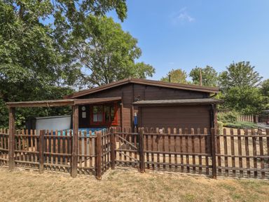 A wooden lodge with a fence and hot tub at Tythe Lodge – Hot Tub Retreat in Rural Lincolnshire | Family-Friendly Lodge Near Heckington