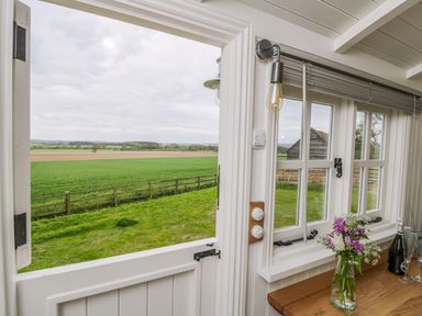A half door open to a grassy field with a wooden fence outside and flowers with a bottle on a wooden countertop inside at Bellwether in Helmsley