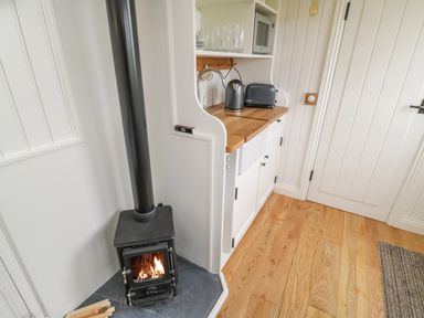 A small wood burning stove with fire next to a kitchenette with kettle toaster and microwave at Bellwether in Helmsley