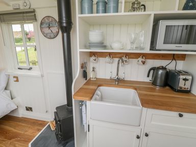 A small kitchen area with a sink kettle toaster microwave dishes and a wood-burning stove at Bellwether in Helmsley