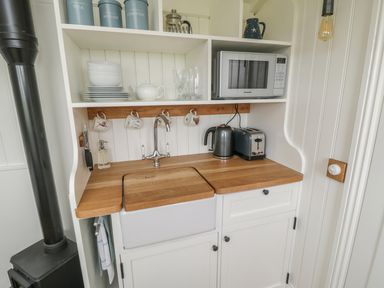 A small kitchen area with a sink microwave kettle toaster and shelves with cups plates and containers at Bellwether in Helmsley