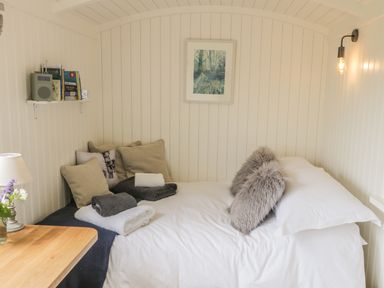 A small bedroom with a bed covered in white and gray bedding and pillows with a wooden table and lamp in the corner at Bellwether in Helmsley