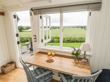 A wooden table with two chairs two glasses of orange juice a plate with croissants a lamp and flowers near an open window and door showing a garden and fields at Bellwether in Helmsley