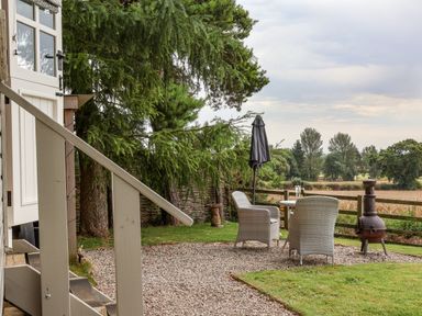 An outdoor seating area with two wicker chairs a small round table with glasses and a bottle a closed umbrella a chiminea and trees in the background at Bellwether in Helmsley