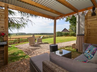 A covered outdoor seating area with wicker furniture and cushions overlooking a garden and countryside at Bellwether in Helmsley