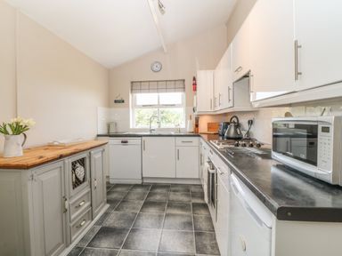 A kitchen with white cabinets a microwave a kettle and a wooden cabinet with flowers at Glasfryn Llanfaethlu