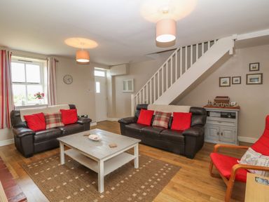 A living room with two leather sofas with red cushions a wooden coffee table a red armchair and stairs at Glasfryn in Llanfaethlu