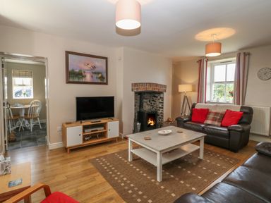A living room with leather sofas a coffee table a television and a wood-burning stove at Glasfryn in Llanfaethlu