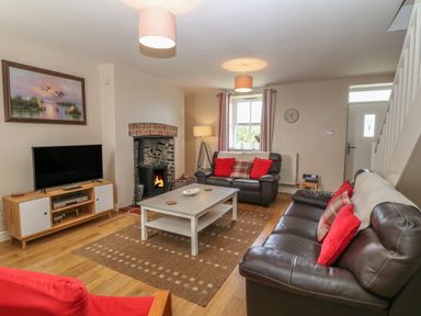 A living room with leather sofas a coffee table a television and a fireplace at Glasfryn in Llanfaethlu