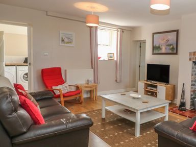 A living room with brown leather sofas a red armchair a white coffee table a television and a fireplace at Glasfryn in Llanfaethlu