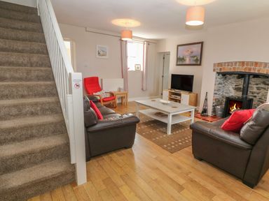 A living room with sofas a coffee table a wood stove and stairs at Glasfryn in Llanfaethlu