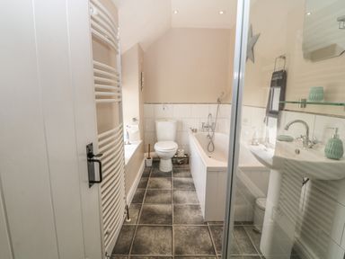 A bathroom with a toilet bathtub sink towel rack and tiled floor at Glasfryn in Llanfaethlu